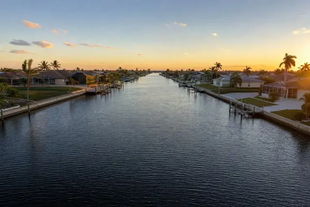 Straight saltwater canal at golden hour lined with concrete seawalls, pool cages, and boat lifts in Cape Coral