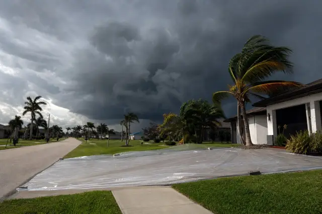 Towering dark storm cloud approaching a flat Cape Coral street where a fresh driveway is covered with plastic sheeting