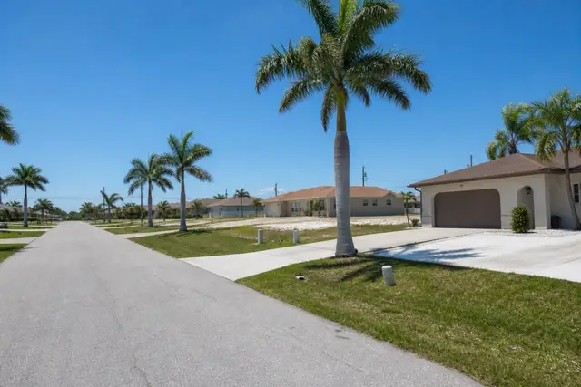Wide Cape Coral residential street under midday sun with royal palms and driveways of different ages