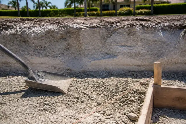 Excavated trench face showing pale gray-white sand layered with crushed shell beneath a Cape Coral work site