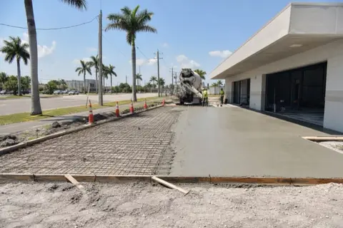 Thick fresh concrete drive apron at a small Cape Coral strip plaza with rebar grid visible in the unpoured half and safety cones along the forms