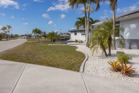 Freshly extruded concrete landscape curbing in a smooth arc between white decorative rock and lawn on a wide Cape Coral street