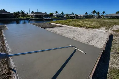Fresh concrete pour in progress inside wooden forms on a Cape Coral canal lot, bull float resting on the wet slab and compacted shell base visible