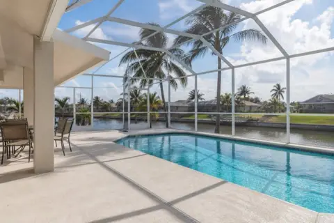 Screened pool enclosure in Cape Coral with pale textured concrete deck, clean drain line, and canal water visible beyond the cage
