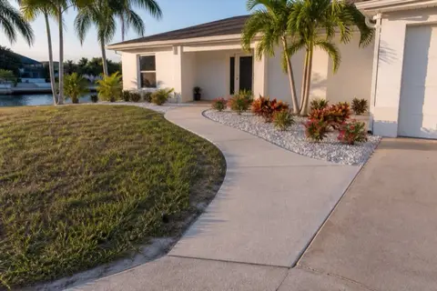 Curved broom-finished concrete walkway leading from a driveway to the covered entry of a white stucco Cape Coral ranch home